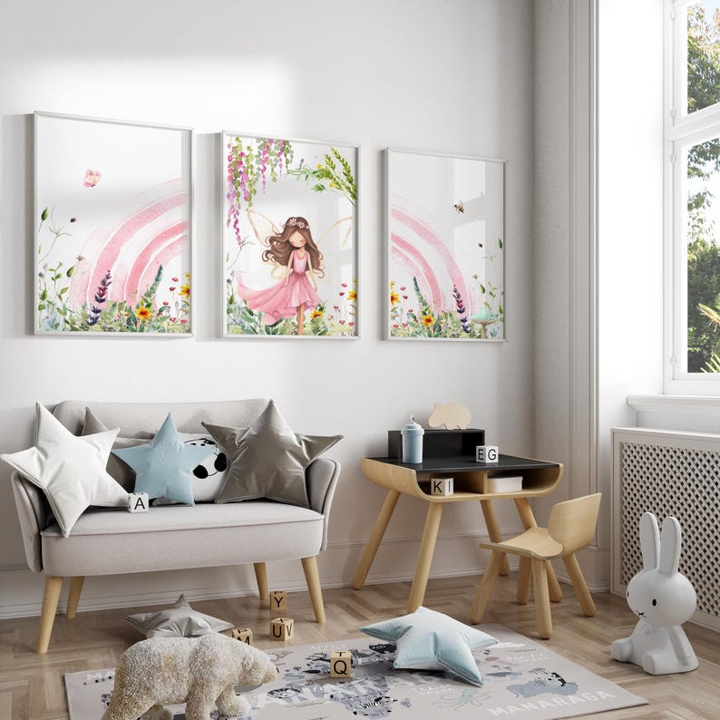 May include: Three watercolor prints featuring a fairy with pink wings and a pink dress standing in a field of flowers with a rainbow in the background. The prints are framed in white and hung on a white wall.