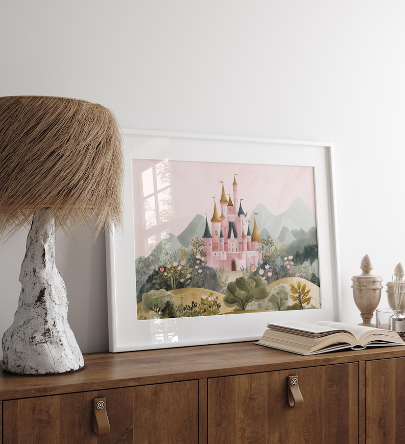 May include: A framed watercolor print of a pink castle with gold and blue turrets, set against a backdrop of green hills and a pink sky. The artwork is displayed on a wooden cabinet, next to a lamp and an open book.