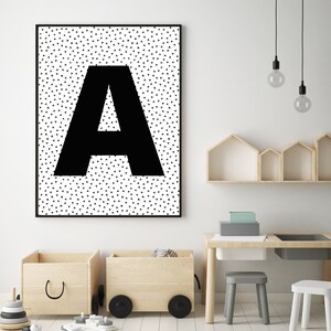 May include: Black framed wall art featuring a large black letter "A" against a white background with small black triangles. The artwork hangs above wooden toy boxes and a small table with a gray stool.