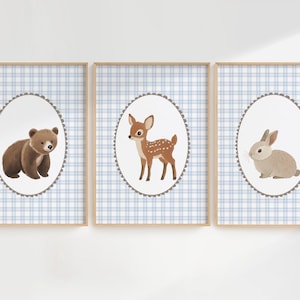 May include: Three framed prints featuring woodland animals. The first print shows a brown bear, the second a deer, and the third a rabbit. Each animal is set against a white oval with a scalloped edge, on a blue and white plaid background.