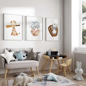 K&ouml;nnte beinhalten: Drei gerahmte Drucke mit Illustrationen einer Giraffe, eines Elefanten und eines Zebras, die Baseball spielen. Die Drucke h&auml;ngen an einer wei&szlig;en Wand &uuml;ber einem hellgrauen Sofa und einem Holztisch mit schwarzer Tischplatte.