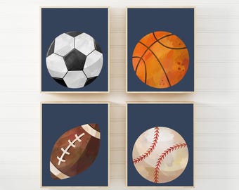 Puede incluir: Cuatro impresiones enmarcadas con balones deportivos. Un balón de fútbol con paneles blancos y negros, un balón de baloncesto naranja, un balón de fútbol americano marrón y un balón de béisbol con costuras rojas, todo sobre un fondo azul marino.