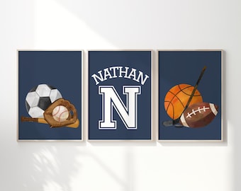 May include: Three framed prints with a navy blue background. One print features a soccer ball, baseball, and glove. Another has the name "NATHAN" above a large white "N". The third print shows a basketball, hockey stick, and football.