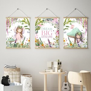 May include: Three framed prints with a whimsical fairy theme. The center print features the text "Dream Big Little One" surrounded by flowers and greenery. The left print shows a fairy with pink wings and a pink dress standing in a forest setting. The right print shows a fairy sitting on a mushroom with a butterfly flying above.