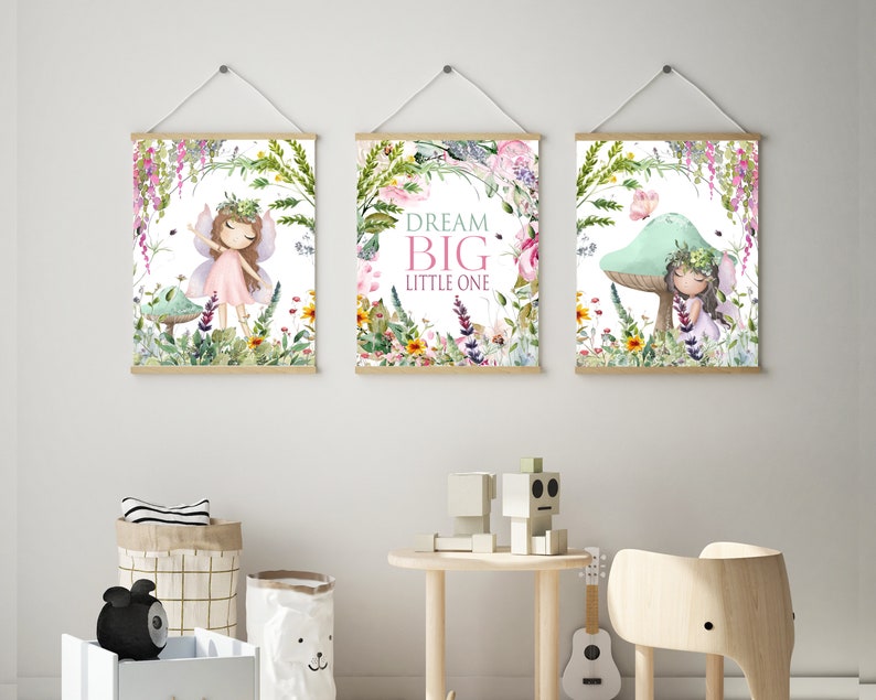 May include: Three framed prints with a whimsical fairy theme. The center print features the text "Dream Big Little One" surrounded by flowers and greenery. The left print shows a fairy with pink wings and a pink dress standing in a forest setting. The right print shows a fairy sitting on a mushroom with a butterfly flying above.