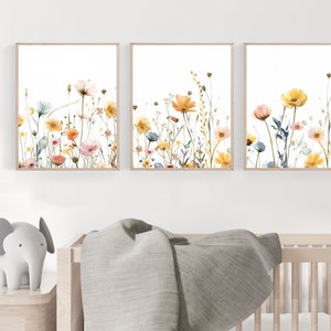 May include: Three watercolor paintings of wildflowers in shades of yellow, orange, pink, and blue on a white background. The paintings are framed in a light wood frame.