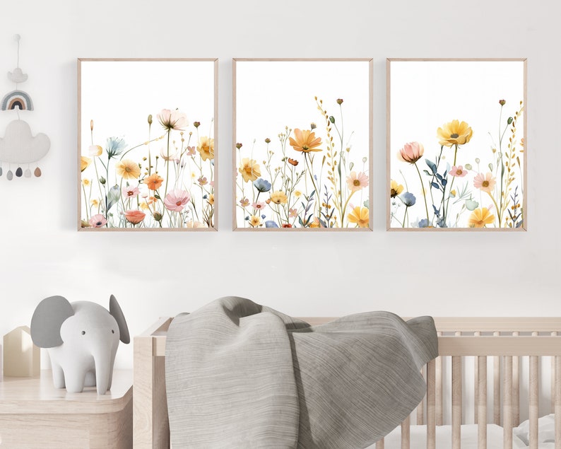 May include: Three watercolor paintings of wildflowers in shades of yellow, orange, pink, and blue on a white background. The paintings are framed in a light wood frame.