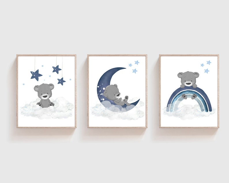 Op de afbeelding: Drie blauwe en grijze kinderkamerprints met een schattige grijze beer op een wolk, een halve maan en een regenboog. De prints zijn perfect voor een babykamer.