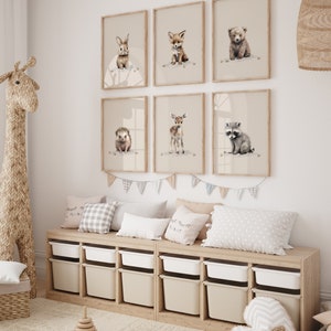 May include: A set of six framed prints featuring watercolor illustrations of baby animals, including a rabbit, fox, bear, hedgehog, deer, and raccoon. The prints are displayed on a white wall above a wooden shelf with storage bins.