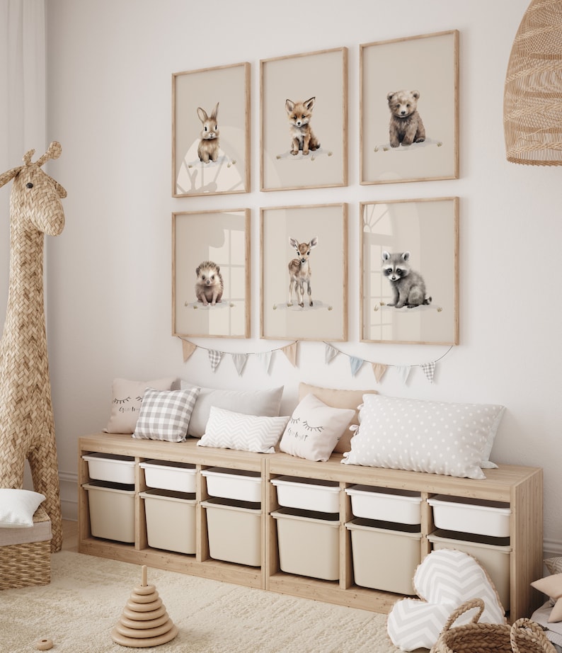 May include: A set of six framed prints featuring watercolor illustrations of baby animals, including a rabbit, fox, bear, hedgehog, deer, and raccoon. The prints are displayed on a white wall above a wooden shelf with storage bins.