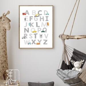 Puede incluir: Un p&oacute;ster de alfabeto enmarcado en blanco con ilustraciones grises, blancas, amarillas, azules y rojas de veh&iacute;culos y se&ntilde;ales de tr&aacute;fico. Las letras est&aacute;n en una fuente gris con un contorno blanco. El p&oacute;ster est&aacute; colgado en una pared blanca.