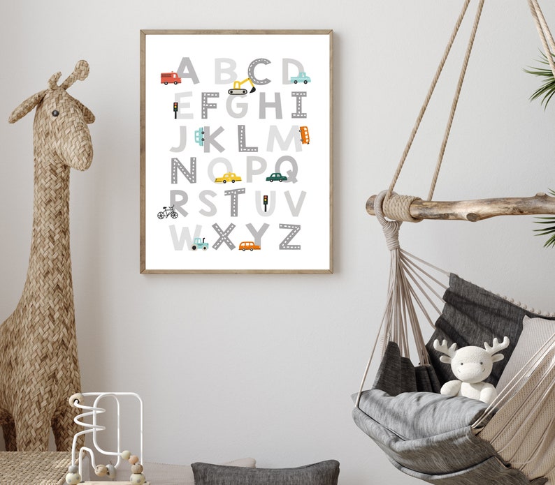 Puede incluir: Un p&oacute;ster de alfabeto enmarcado en blanco con ilustraciones grises, blancas, amarillas, azules y rojas de veh&iacute;culos y se&ntilde;ales de tr&aacute;fico. Las letras est&aacute;n en una fuente gris con un contorno blanco. El p&oacute;ster est&aacute; colgado en una pared blanca.