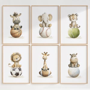 May include: Set of six framed watercolor prints featuring adorable baby animals. A zebra, elephant, and tiger sit atop a basketball, baseball, and tennis ball. A lion, giraffe, and hippo sit on a soccer ball, football, and golf ball.