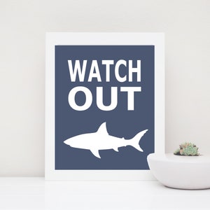 Op de afbeelding: Een wit silhouet van een haai op een donkerblauwe achtergrond met de tekst "WATCH OUT" in wit.