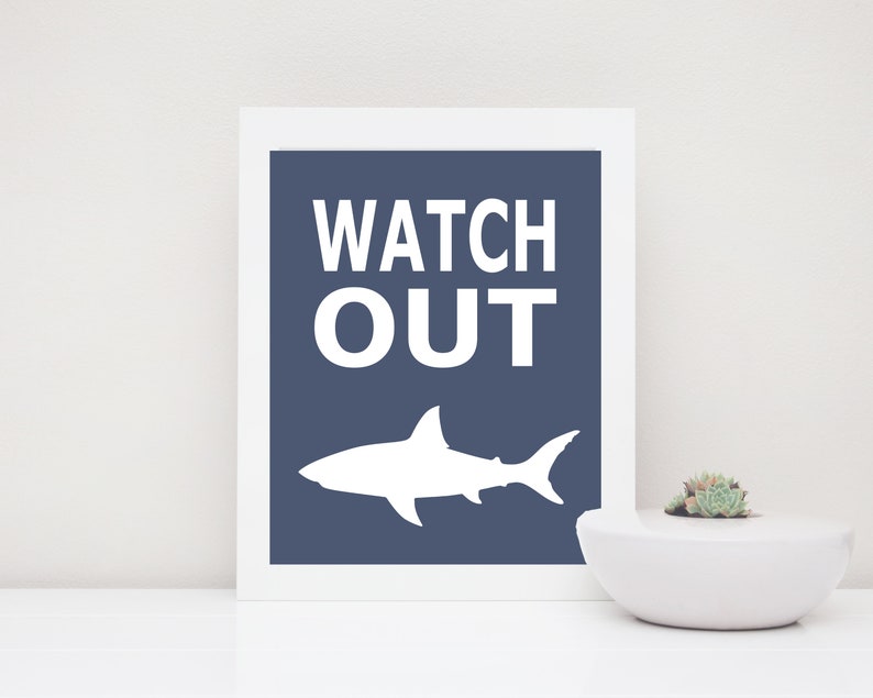 Op de afbeelding: Een wit silhouet van een haai op een donkerblauwe achtergrond met de tekst "WATCH OUT" in wit.