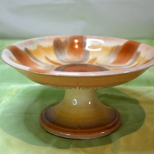 May include: A ceramic pedestal bowl with a swirl pattern in shades of brown, orange, and white.