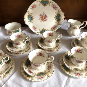 Puede incluir: Un juego de té vintage con tazas, platillos y una fuente de porcelana blanca, adornado con diseños florales en rosa, amarillo y azul. El juego incluye una jarra para crema y un azucarero.