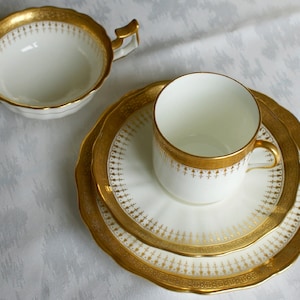 Pode incluir: Um conjunto de chávena e pires de chá branco com guarnição dourada e um padrão floral delicado. O conjunto é feito de porcelana fina e é perfeito para um chá formal.