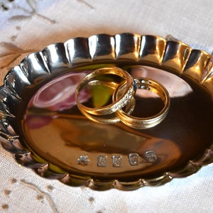 Peut inclure: Deux alliances en or, l'une sertie de petits diamants, reposant sur un plat en argent à bord festonné.