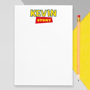May include: A white notepad with the text "KEVIN STORY" in yellow and red, with a pencil to the right. The notepad is on a gray and yellow background. The pencil is yellow with a pink eraser.