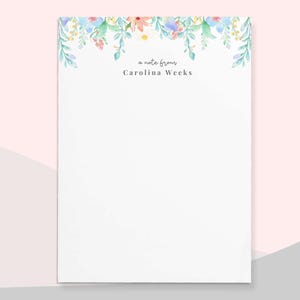 May include: White stationery with a floral border in pastel colors. The text "a note from" and "Carolina Weeks" are printed in black. The bottom of the stationery has the website address "www.paperandclips.co" and the Paper & Clips Co. logo.