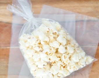 May include: A clear plastic bag filled with white popcorn. The bag is sitting on a wooden surface.