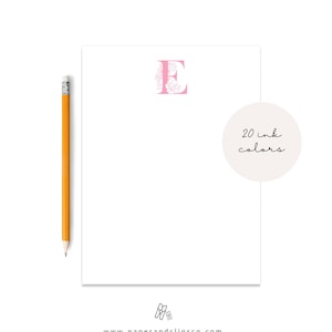 May include: A white notepad with a pink letter E with floral details. The notepad has a circle with the text "20 ink colours" on the bottom right corner. The website address "www.paperandclipsco.com" is printed at the bottom of the notepad.