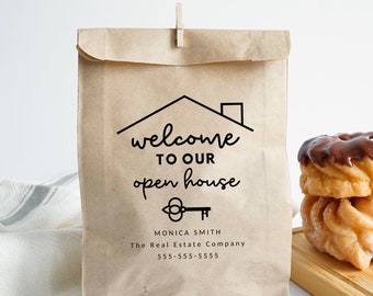May include: A brown paper bag with a welcome to our open house sign. The sign features a house icon and a key. The bag is 5 inches by 8 inches. Monica Smith, The Real Estate Company, 555-555-5555.