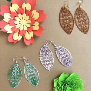 May include: An assortment of handmade leaf-shaped earrings in brown, green, and purple, with intricate lace-like designs. Decorative paper flowers in red, yellow, and green are also present, creating a craft-focused theme.