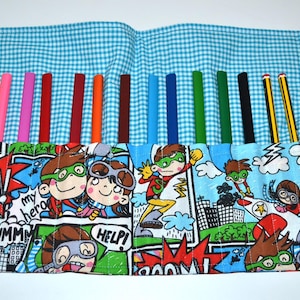 Könnte beinhalten: Buntes Stiftetui mit einem Superhelden-Comic-Design. Das offene Etui zeigt verschiedene Buntstifte und zwei Bleistifte. Das Etui besteht aus blauem Vichy-Stoff und hat eine blaue Kordel zum Zubinden.