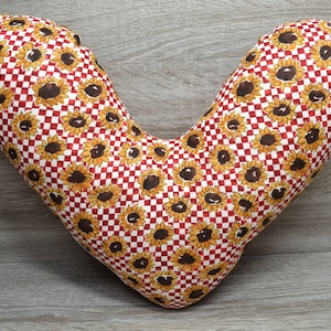 Könnte beinhalten: Ein herzförmiges Kissen mit einem rot-weiß karierten Muster und einem Sonnenblumen-Druck.