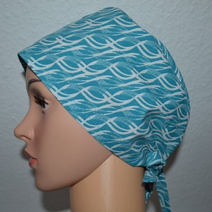 May include: A teal blue surgical scrub hat with a white wave pattern. The hat has a tie at the back.