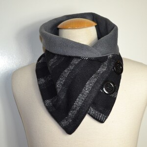 Könnte beinhalten: Ein schwarz-grau gestreifter Cowl-Neck-Schal mit zwei großen schwarzen Knöpfen. Der Schal wird auf einer Schaufensterpuppe präsentiert und hat einen grauen Kragen. Der Schal ist aus einem weichen, warmen Material gefertigt.