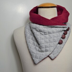Può includere: Un foulard a collo a scialle trapuntato grigio e bordeaux con bottoni marroni. Il foulard è realizzato in un tessuto morbido e confortevole ed è perfetto per tenersi al caldo in inverno.