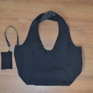 Puede incluir: Un bolso tote negro con una pequeña bolsa y un cordón a juego. Las asas del bolso y el cordón presentan un estampado de lunares blancos sobre fondo negro. El bolso y la bolsa están hechos de tela negra lisa.