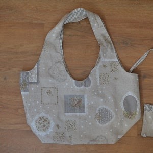 May include: Beige tote bag and matching small pouch. The bag has a wide, curved handle and is decorated with floral and heart patterns. The pouch has a small strap and a zip closure. Both items are made of fabric.