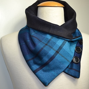 Könnte beinhalten: Ein blau-schwarzer Schal mit schwarzem Kragen und drei schwarzen Knöpfen. Der Schal wird auf einer Schaufensterpuppe präsentiert und hat eine dreieckige Form. Das Karomuster weist Blau- und Schwarztöne auf.