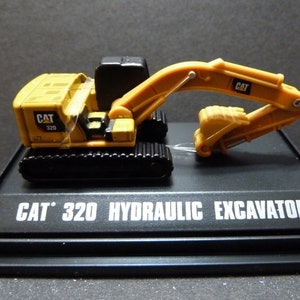 May include: A yellow and black CAT 320 hydraulic excavator model. The model features a detailed design with a movable arm and bucket. The base of the model has the text "CAT 320 HYDRAULIC EXCAVATOR" in white.
