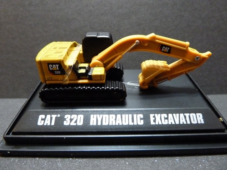 May include: A yellow and black CAT 320 hydraulic excavator model. The model features a detailed design with a movable arm and bucket. The base of the model has the text "CAT 320 HYDRAULIC EXCAVATOR" in white.