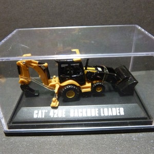 May include: A miniature CAT 420E backhoe loader model, predominantly black and yellow, encased in a clear display case. The model sits on a black base with the text "CAT 420E BACKHOE LOADER". The backhoe arm is extended.