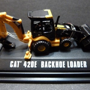 May include: A miniature CAT 420E Backhoe Loader model. The construction vehicle is black and yellow, with a detailed design. The model sits on a black base with the text "CAT 420E BACKHOE LOADER" in white.