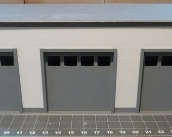 Puede incluir: Un modelo de edificio blanco con tres puertas de garaje grises. Las puertas tienen cuatro ventanas rectangulares cada una.