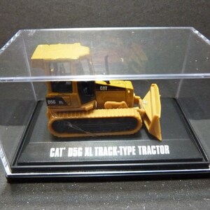 May include: A yellow and black CAT D5G XL track-type tractor model is displayed in a clear acrylic case. The model features a blade and track design, with the text "CAT D5G XL TRACK-TYPE TRACTOR" on the base.