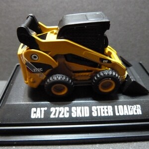 May include: A yellow and black CAT 272C skid steer loader model. The model has black tires, a black cab, and a black bucket. The text "CAT 272C SKID STEER LOADER" is printed in white on the black base.