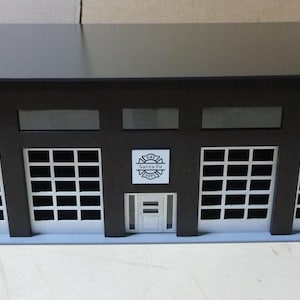 May include: A model of a building with a black roof, brown walls, and white garage doors. The building has red brick accents on the sides and a white door in the center. The text "Santa Fe" is visible above the door.