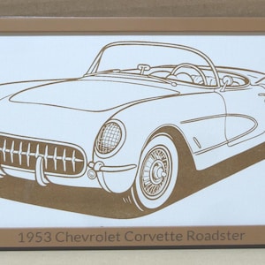 May include: A framed print featuring a detailed line drawing of a 1953 Chevrolet Corvette Roadster. The car is depicted in a side view with visible wheels, headlights, and interior details. The text "1953 Chevrolet Corvette Roadster" is at the bottom.