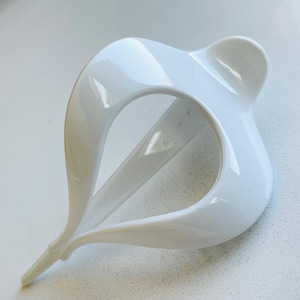 May include: A glossy white hair accessory featuring a curved, open-loop design that tapers to a pointed end. The structure consists of smooth, interconnected arcs forming a central void, creating a sleek, sculptural shape with a reflective finish.