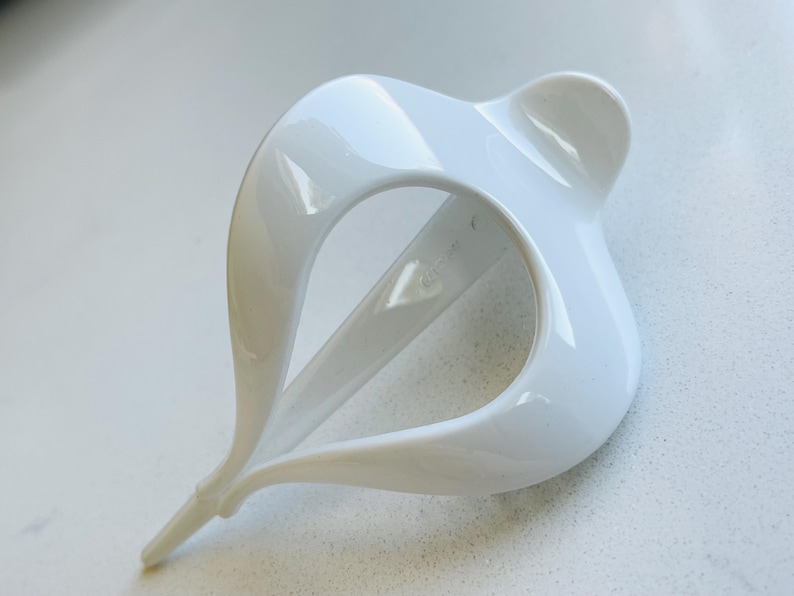 May include: A glossy white hair accessory featuring a curved, open-loop design that tapers to a pointed end. The structure consists of smooth, interconnected arcs forming a central void, creating a sleek, sculptural shape with a reflective finish.