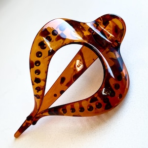 May include: A teardrop-shaped hair clip featuring a glossy, translucent amber and dark brown tortoiseshell pattern. The accessory has a smooth, curved frame with a central open space and a pointed tip, showcasing a polished finish throughout.