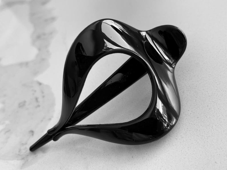 May include: A glossy black hair clip with a smooth, curved, teardrop-shaped frame. The accessory features an open center design with a pointed end and a rounded, wider base, showcasing a reflective surface and a solid, dark, monochromatic finish.